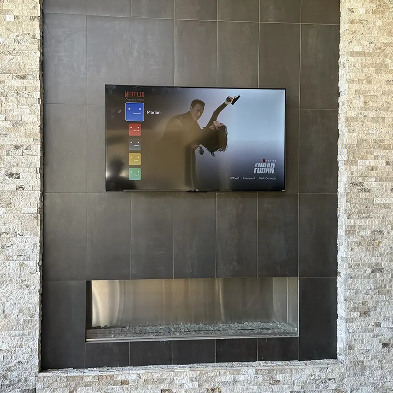 Outdoor TV mounted above stone tile fireplace, outlet hidden behind for clean look