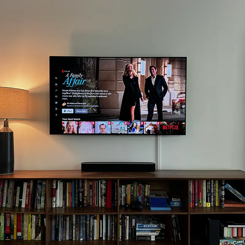 TV mounted above bookshelf with soundbar on top, cables in white cord cover